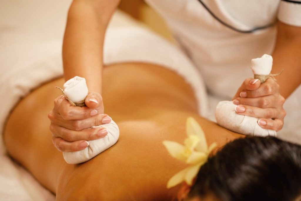 Ayurvedic therapist performing herbal pouch massage (Kizhi therapy) on a patient's back during a traditional Panchakarma treatment session.